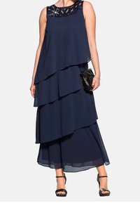 Annaver navy layered maxi dress with a beaded neckline, sheer chiffon fabric, and a flowing silhouette, paired with a black clutch and heels.
