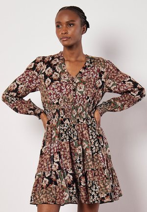 Bloemenjurk met lange mouwen en V-hals, met een gesmokt taille, gelaagde rok en een donkere achtergrond met multkleurige bloemenpatronen.