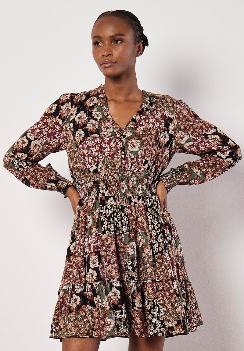 Vestido floral con mangas largas y escote en V, que presenta una cintura fruncida, falda de volantes y un fondo oscuro con patrones de flores multicolores.