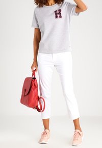 Grå kortärmad t-shirt med ett mönstrat "H"-patch, ihop med vita cropped byxor, rosa sneakers och en röd läderryggsäck.