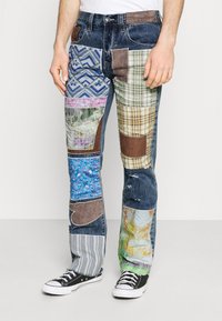 Jeans de mezclilla patchwork que presentan varios materiales y patrones, incluyendo cuadros, flores y rayas, con secciones desgastadas y corte recto.