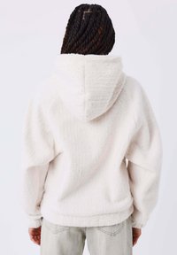 Sudadera con capucha blanca y texturizada en un material suave con un corte holgado, que presenta detalles acanalados y una silueta acogedora y oversized.