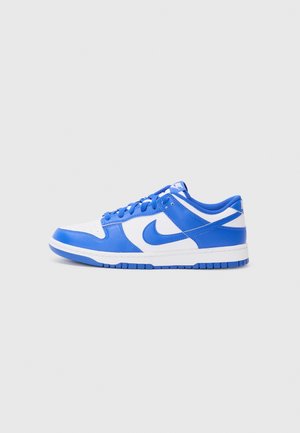 Lavtop-sneaker i blå og hvidt læder med blå snørebånd og Nike-swoosh, set fra siden på en ensfarvet lysegrå baggrund.