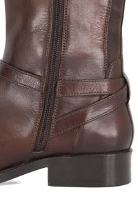 Brown leather ankle boot featuring a side zipper, textured finish, decorative strap accents, and a low, sturdy black heel.