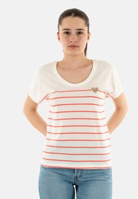 Camiseta blanca de algodón con rayas corales horizontales, escote redondeado y mangas cortas; presenta un pequeño adorno en forma de corazón dorado en el pecho.