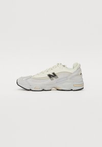 Zapatillas deportivas blancas con materiales superpuestos que incluyen malla y ante. Presenta un logo negro, acentos texturizados y una suela gruesa y acolchada.