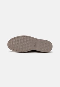 Semelle de chaussure en caoutchouc, présentant une surface texturée avec des motifs en losange et une couleur beige. Le nom de la marque est embossé sur le côté.