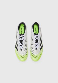 Zapatillas de fútbol blancas y negras con parte superior texturizada, detalles en verde y suela con patrón. Cuentan con cordones y un marcado branding en el interior.