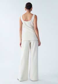 Lichtbeige mouwloze top met een ronde rug, gecombineerd met een brede broek in een bijpassende kleur, gemaakt van een gemêleerde stof.