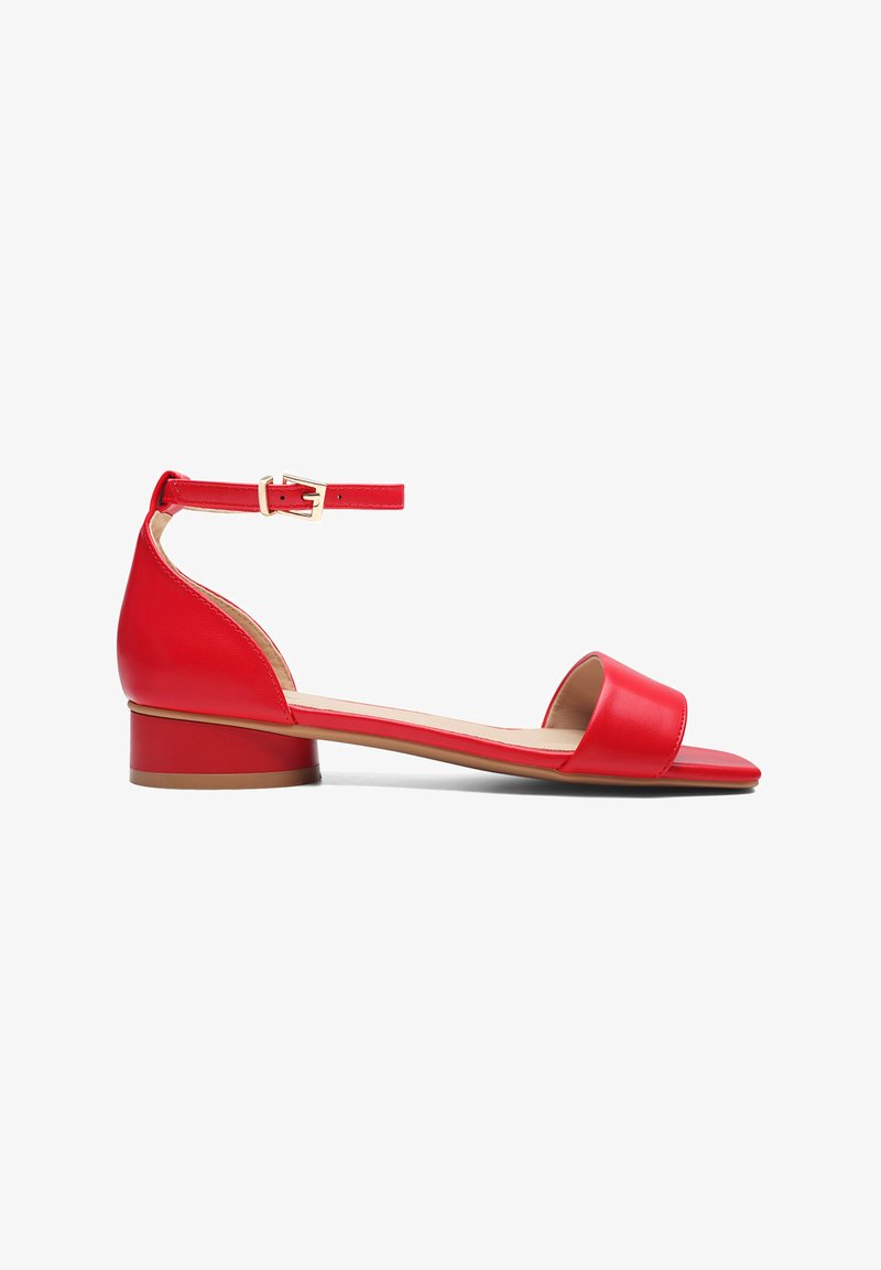 Sandale en cuir rouge au design minimaliste, avec une large bande au niveau des orteils, une bride de cheville avec une boucle et un petit talon carré.