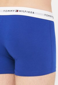 Blaue Baumwoll-Boxershorts mit weißem Bund, der das "TOMMY HILFIGER"-Logo sowie rote und weiße Akzente zeigt. Glatte Textur und taillierte Passform.