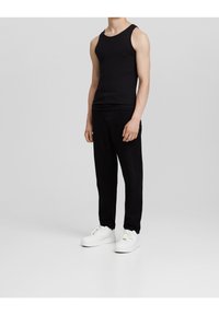 Top sin mangas negro combinado con pantalones ajustados negros y zapatillas blancas, todo sobre un fondo neutro. Diseño simple y limpio.