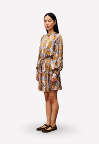 Braunes und blaues gemustertes Kleid mit langen Ballonärmeln, einer taillierten Taille und einem ausgestellt Rock, kombiniert mit braunen Mary Jane Schuhen.