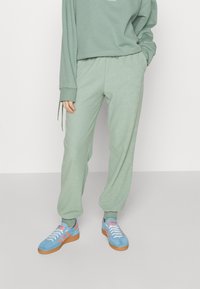 Mintgrön, texturerad sweatshirt och matchande joggers. Sneakers har blå mocka med rosa ränder och bruna gummisålar.