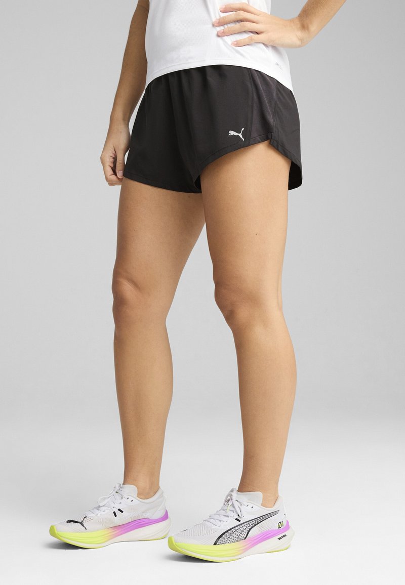 Black athletic shorts with a loose fit, contrasting white logo, paired with white running shoes featuring a gradient purple and yellow sole.