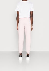 Ljusrosa sweatshirtbyxor med elastiska muddar, tillverkade av mjukt tyg. Bärs med en vit, löst sittande t-shirt, sedd bakifrån.