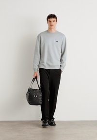 Sudadera gris clara con puños acanalados, combinada con pantalones negros. El modelo lleva un bolso negro con un acento metálico circular.