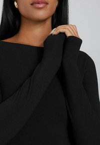 Schwarzes Langarmshirt mit weitem Ausschnitt, aus glattem Stoff gefertigt. Eng anliegende Ärmel mit einer angenehmen Haptik, die teilweise die Hände bedecken.