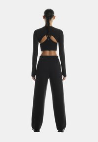 Black long-sleeve crop top with cutout back design. Paired with wide-leg black pants. Smooth texture, fitted silhouette, minimalist style.