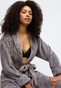 Pilkas, minkštas, fliso chalatas su šalių apykakle, surišamu liemeniu ir šoninėmis kišenėmis. Turi ilgomis rankovėmis ir laisvą kirpimą.