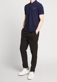 Marine polo med korte ærmer, ribbet krave og broderet logo. Sammen med sorte bukser og hvide sneakers. Subtil tekstur.