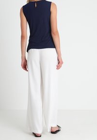 Un haut sans manches bleu marine avec une découpe en forme de trou de serrure dans le dos ; associé à un pantalon blanc ample et des chaussures plates noires.