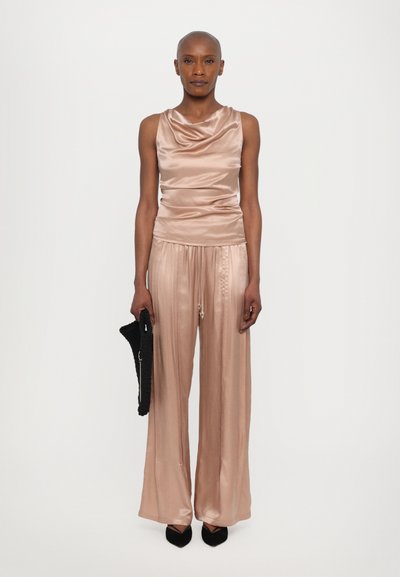 Canotta in satin con colletto drappeggiato in rosa abbinata a pantaloni palazzo plissettati. Accessori: pochette nera texturizzata, ballerine nere appuntite.