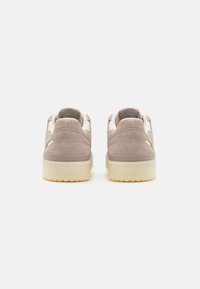 Ljusbruna sneakers i mocka med en krämfärgad detalj, utrustade med en vadderad krage, platta snören och en tjock, strukturerad gummisula.