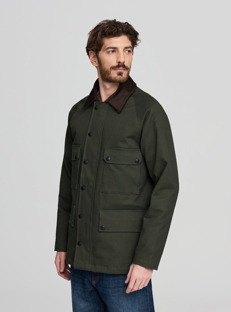 Giacca verde oliva con chiusura a bottoni, colletto in velluto a coste marrone e quattro tasche frontali. Tessuto liscio con design strutturato.
