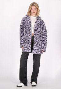 Abrigo de piel sintética de leopardo morado con botón frontal, solapas anchas y mangas largas, combinado con jeans de pierna ancha negros y zapatillas blancas.