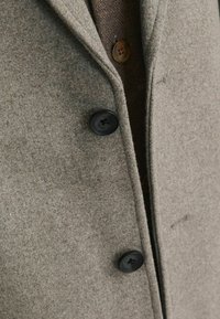 Palton gri din lână cu o textură moale, având un guler tăiat, două butoane negre și o căptușeală interioară din tweed maro.