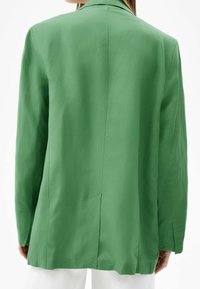 Groene blazer met een gladde textuur, enkele achterventilatie en lange mouwen. Eenvoudige revers en gedetailleerde stiksels accentueren het ontwerp.