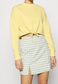 Sweat-shirt court jaune à manches longues, associé à une mini-jupe à motif vichy vert et blanc avec une fente latérale.