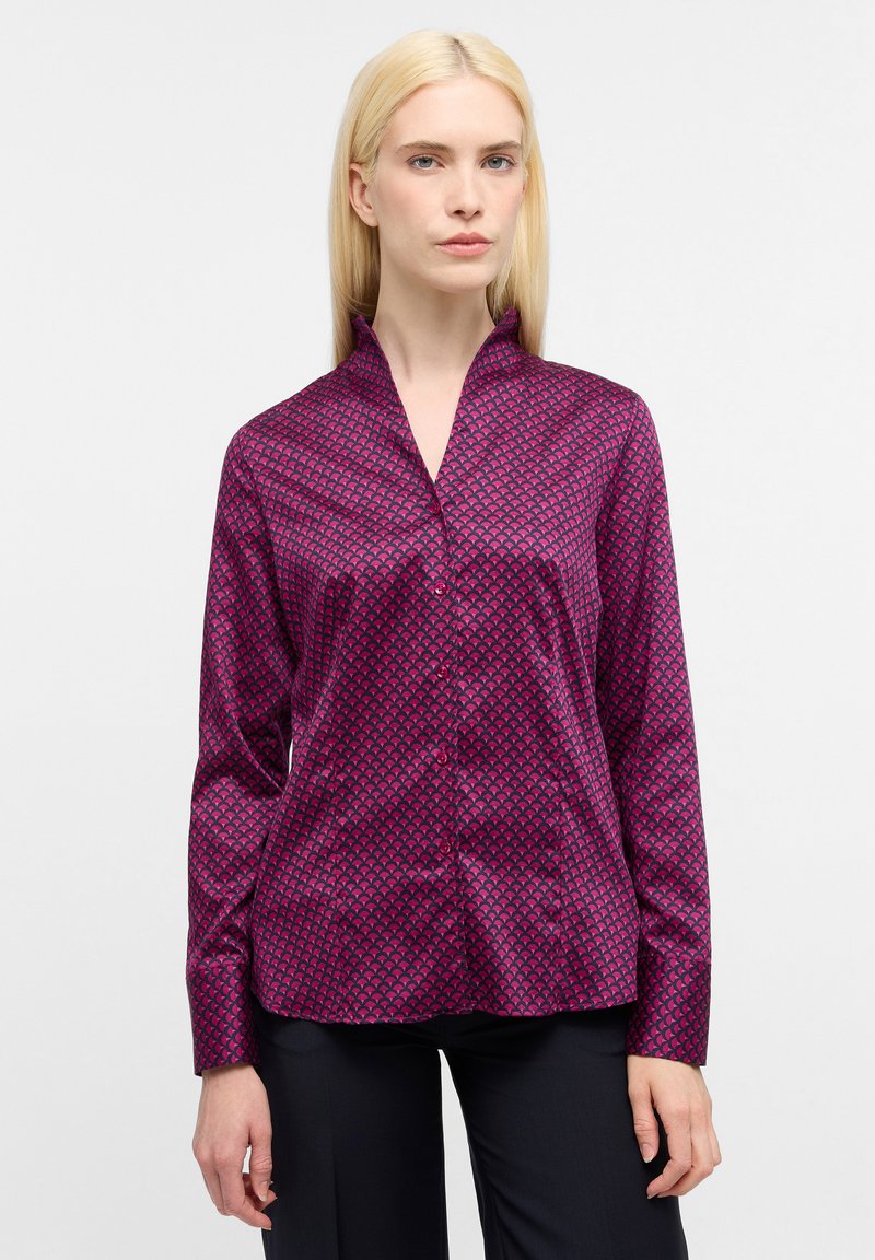 Blusa fucsia con un motivo geometrico, dotata di maniche lunghe, chiusura con bottoni sul davanti e colletto alla mandarino. Tessuto liscio e testurizzato.