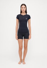 Svart treningsgenser med korte ermer, med glidelås foran og et logo. Kombinert med tettsittende svarte shorts. Glatt, stretchy stoff.