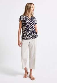 Short-sleeve, lightweight top with a black and white abstract zebra print, paired with relaxed-fit, cream-colored trousers and flat sandals.