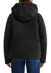 Zwarte pufferjack met een capuchon, textiele stof, achternaad en twee zijzakken, gecombineerd met blauwe spijkerbroek.