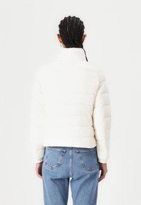 Hvit dunjakke med høy krage, quiltet design og elastiske ermer, parret med blå denimjeans med baklommer.