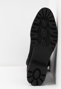 Suola di scarpa nera con superficie in gomma testurizzata; presenta un design robusto con motivi circolari e battistrada pronunciato per una migliore aderenza.