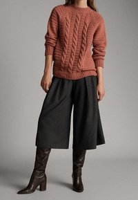 Rdzawy sweter z dzianiny w warkocze w kolorze przybrudzonego różu, w zestawieniu z ciemnymi, szerokimi kulotami oraz brązowymi, wysokimi botkami na obcasie. Teksturowany i warstwowy design.