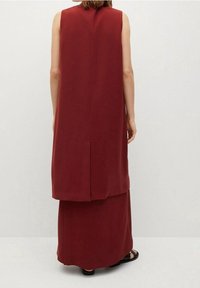 Burgundy bezramenné šaty s dlouhou sukní, obsahující ventilační otvor na zadní straně. Hladká textura, minimalistický design a silueta až po kotníky.