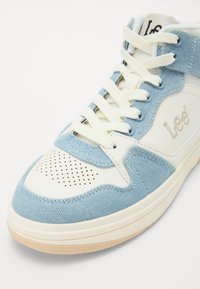 Tênis de cano alto com uma mistura de denim azul claro e material sintético branco, bico redondo, detalhes perfurados e solas de borracha bege.