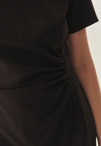 Vestido negro entallado con mangas cortas, que presenta detalles fruncidos en el costado, textura suave y una silueta elegante.
