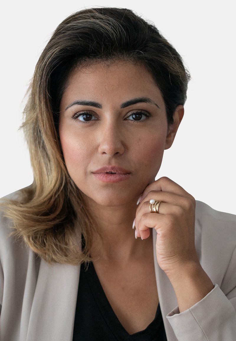 Portrett av en kvinne med middels brunt hår, iført en lys beige blazer over en svart topp. Merkbare gullringer på fingrene hennes.