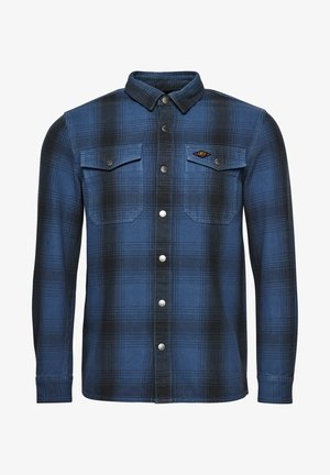 Camisa de cuadros azul y negra de manga larga con botones, dos bolsillos en el pecho, botones de presión y un pequeño parche con el logo "DRY" en el bolsillo izquierdo.
