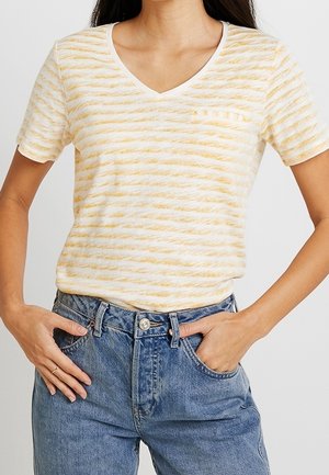 Kvinde iført en gul- og hvidstribet V-hals T-shirt med en lille lomme, stoppet ind i højtaljede blå denimjeans.