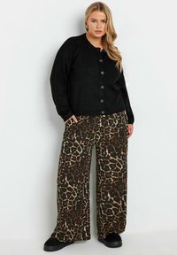 Svart kofta med rund halsringning och stora knappar, tillsammans med vida leopardmönstrade byxor i brunt och svart. Svarta slip-on skor.