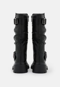 Para czarnych skórzanych butów za kostkę z grubymi obcasami, bocznymi klamrami i suwakami, widoczna z tyłu na białym tle.