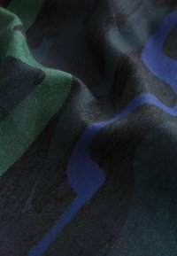 Primo piano di un tessuto con un motivo mimetico scuro caratterizzato da forme astratte verdi, nere e blu e una trama intrecciata visibile.