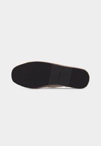Semelle d'une chaussure décontractée sans lacets avec une semelle en caoutchouc noir et des bords tissés beiges, arborant un patch rectangulaire du logo Calvin Klein au centre.